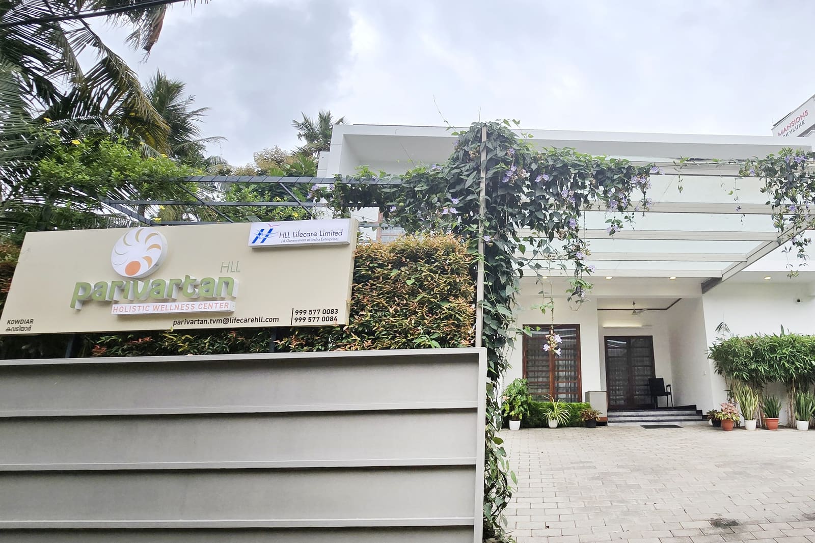The Parivartan Holistic Wellness Center in Kowdiar, Trivandrum — its signboard beside the plant-lined, flowering entrance porch