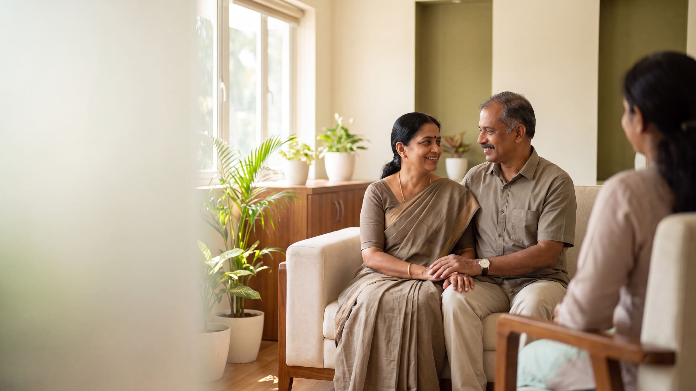 A senior couple sharing a warm moment during a counselling session in a bright, plant-filled room